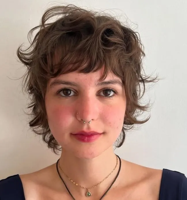Pixie mullet frizura za pravokotni obraz – kombinacija kratkih plasti in razmršene teksture, ki mehča poteze.