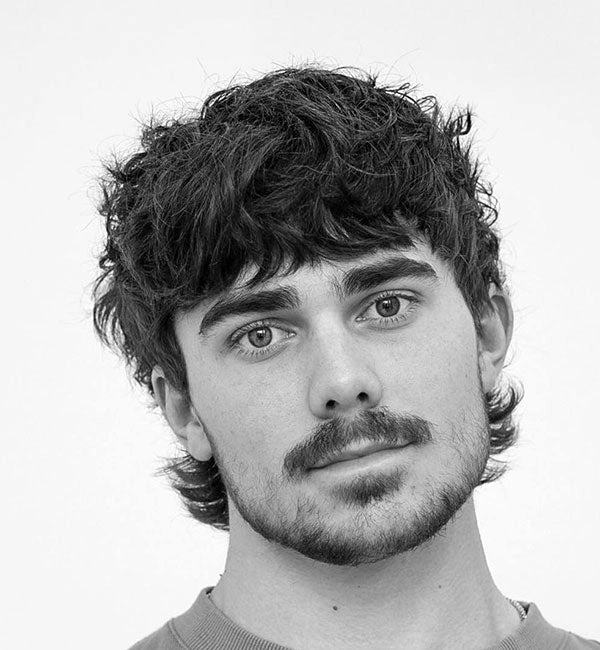 Srednje dolga moška mullet frizura z gostim frufrujem in razmršenim videzom.